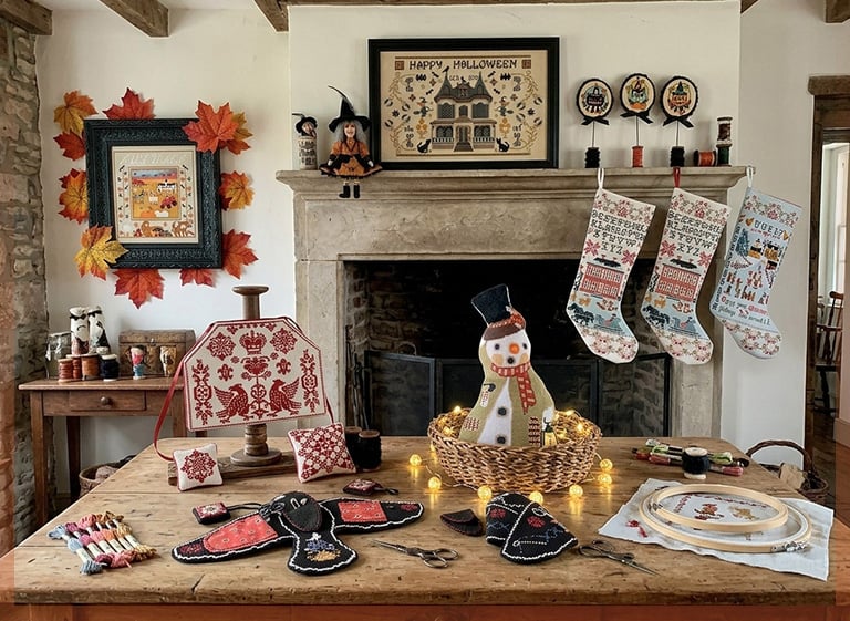 Twin Peak Primitives cross stitch designs and accessories: 'Happy Halloween' sampler, stitched stockings, scissor fobs and pincushions on a rustic table.